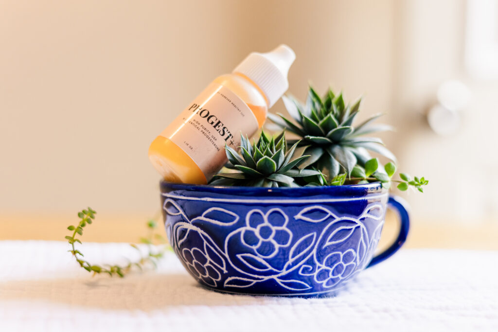 Progesterone on top of succulent plant in blue tea cup sitting on white linen, side view