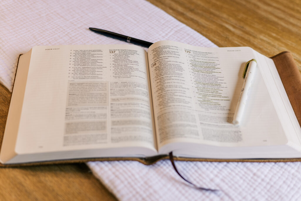 Bible open with pen and highlighter sat on white linen on a light hard wood table